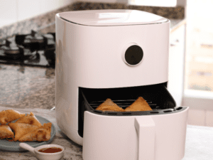 A white air fryer with two samosas inside the basket.