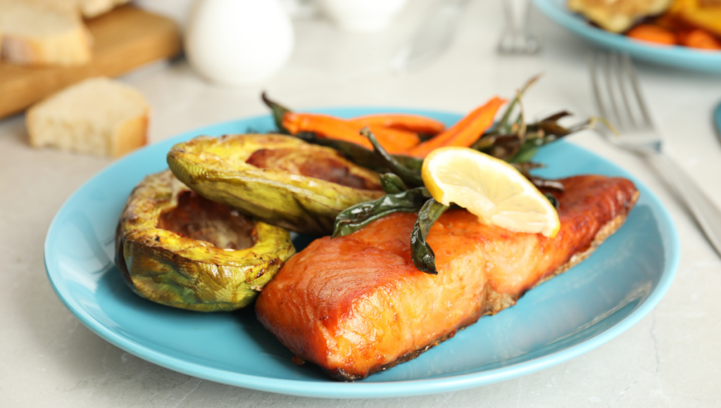 A plate of salmon filet air-fried to a crisp, served with roasted zucchini and carrots, garnished with a lemon slice.