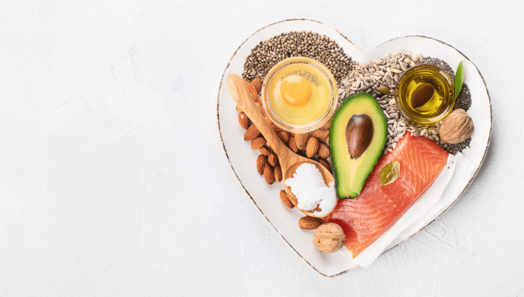 A heart-shaped plate featuring avocado, salmon, seeds, nuts, and a raw egg, all nutrient-dense superfoods.