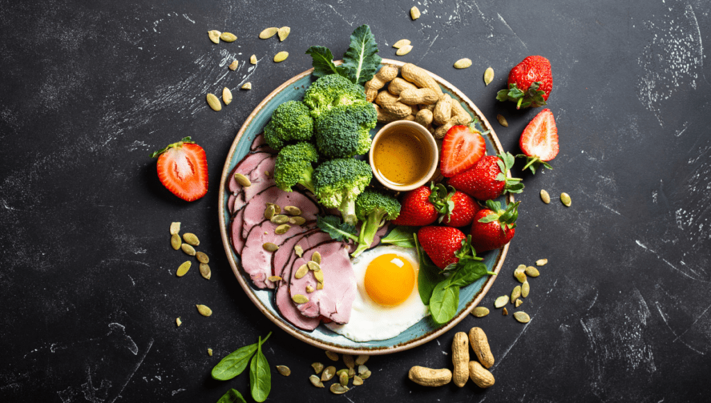 A nutritious breakfast plate with ham, broccoli, egg, and strawberries, garnished with peanuts.