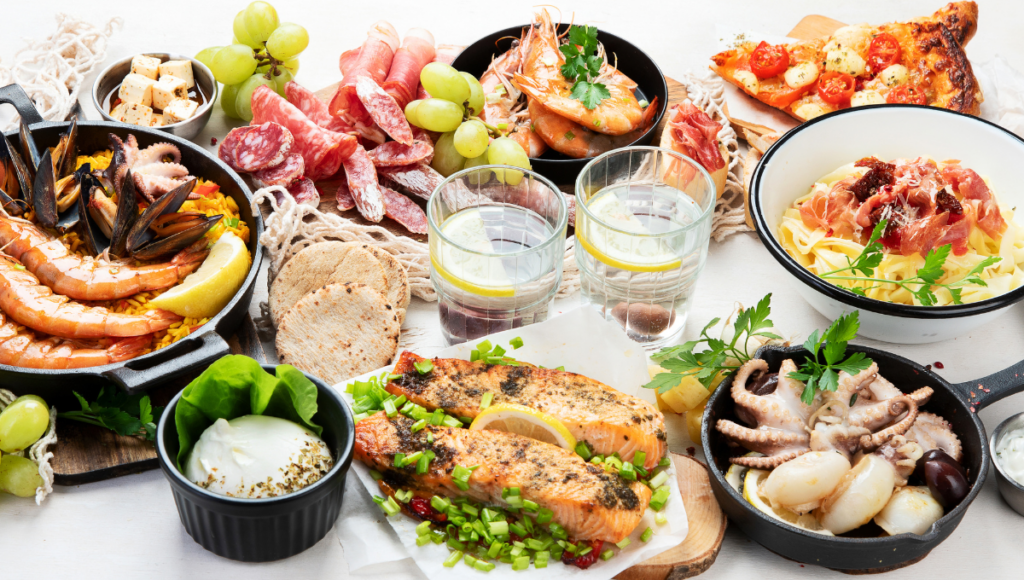 A table filled with Mediterranean seafood, appetizers, and fresh bread, including shrimp, salmon, and octopus, paired with salads and sauces.