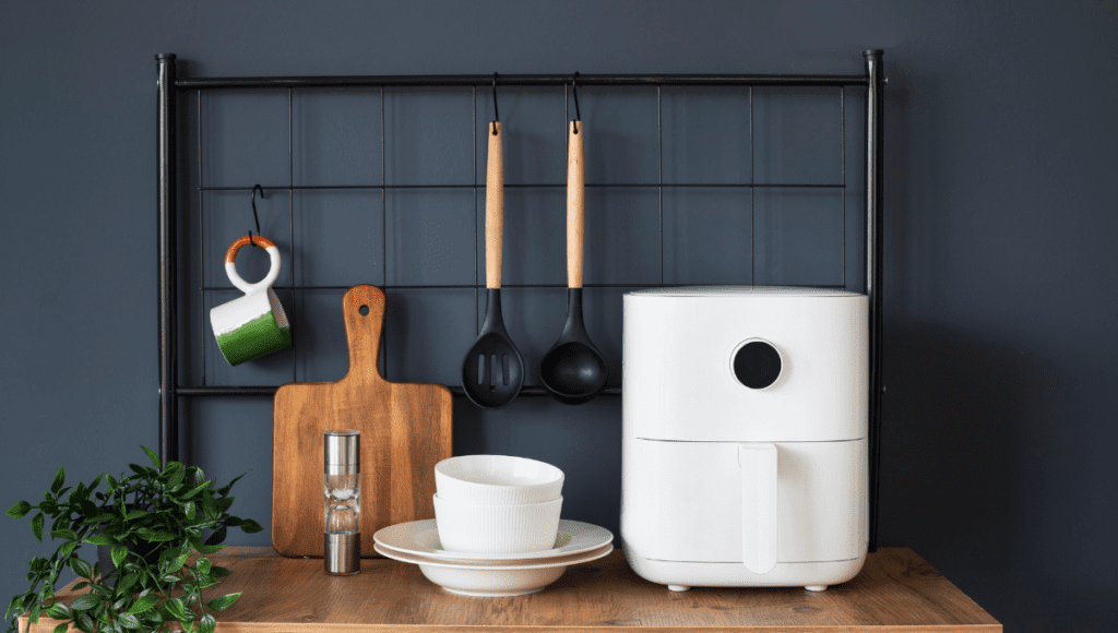 A white air fryer placed on a wooden shelf with bowls and kitchen utensils neatly arranged around it.