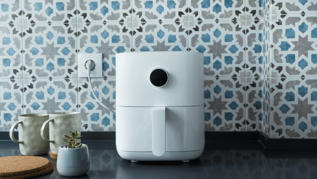 White air fryer on a tiled kitchen counter beside mugs and a succulent plant.