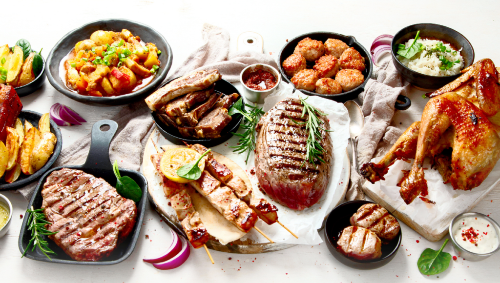 A beautifully arranged table filled with a variety of grilled meats, ribs, steak, roasted chicken, and sides like roasted potatoes and vegetables.