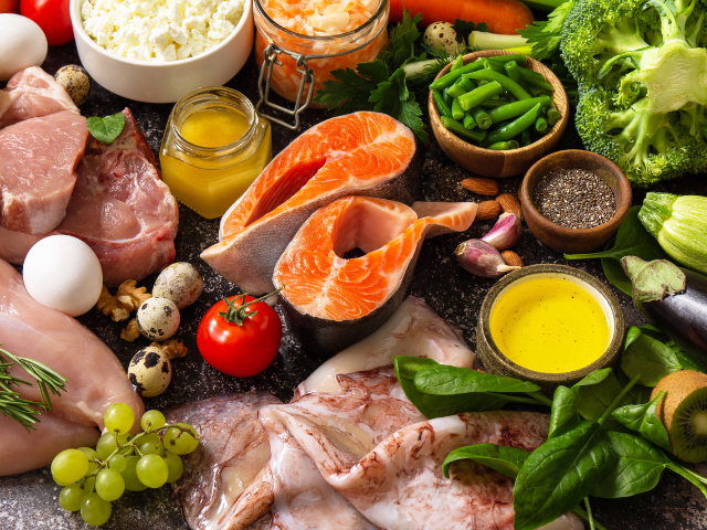 A display of Mediterranean ingredients including fresh salmon, chicken, vegetables, eggs, and olive oil, all placed on a kitchen countertop.