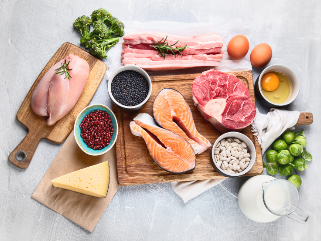 A selection of raw ingredients including chicken, salmon, beef, eggs, cheese, and fresh vegetables displayed on a kitchen counter, ready to be prepared.