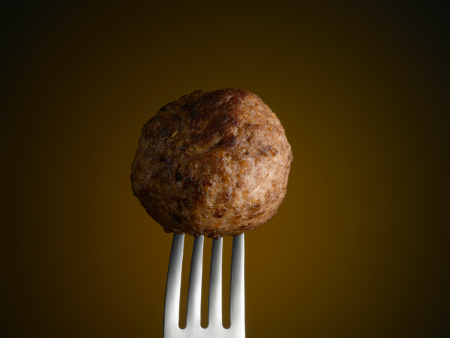 A perfectly cooked, juicy meatball balanced on a fork, ready to be enjoyed.