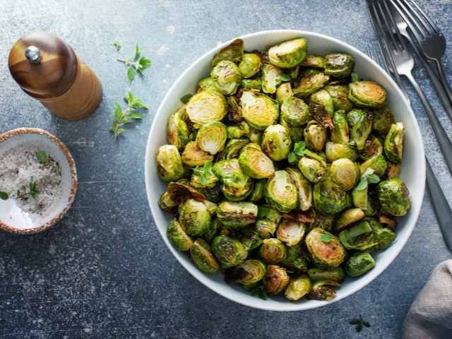 A bowl of perfectly roasted Brussels sprouts, garnished with herbs and served on a rustic table.