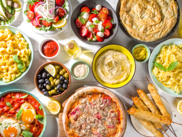 A variety of Mediterranean foods such as salads, pizza, hummus, olives, and fresh vegetables, laid out on a table for a meal.