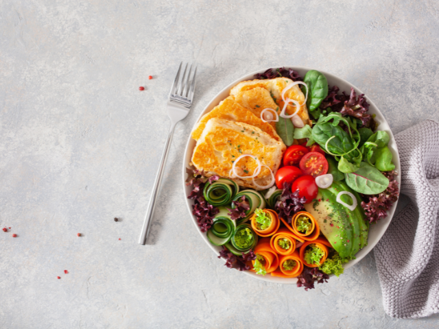 A plate filled with fresh greens, sliced vegetables, and fried eggs arranged neatly with a fork placed on the side.