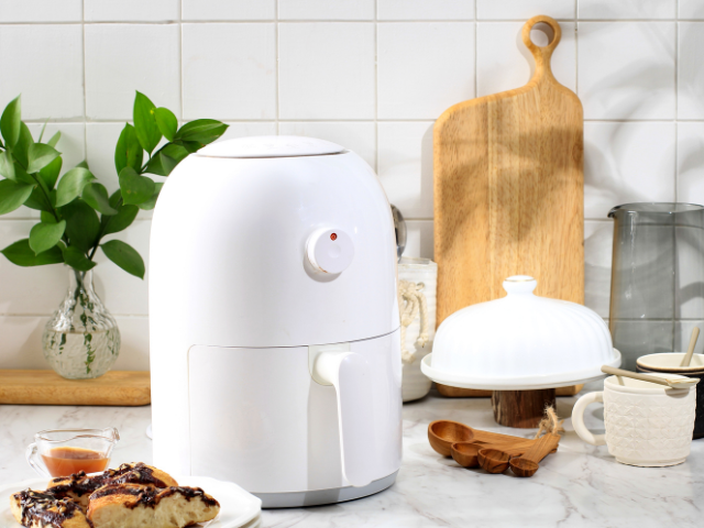 A white air fryer placed on a marble countertop in a modern kitchen with cooking utensils around it.