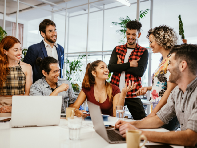 A group of diverse people in a professional office environment engaged in a friendly discussion, showing teamwork and collaboration.