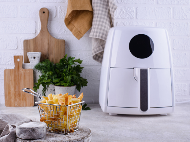 White air fryer beside a basket of crispy fries in a cozy kitchen.