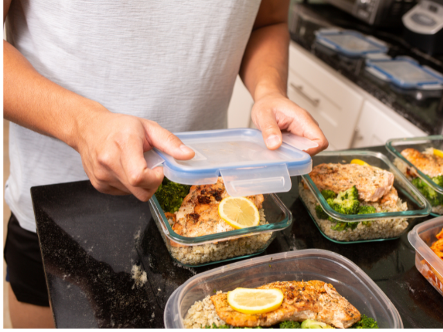 A person preparing meal containers with cooked salmon, broccoli, and rice in glass containers, ready for storage.