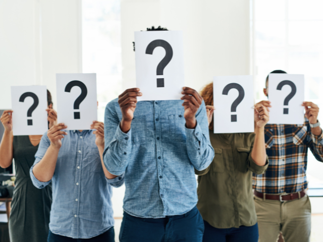 A group of people holding papers with question marks covering their faces.