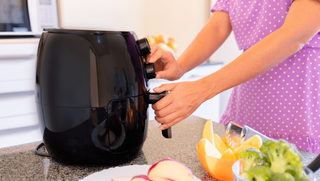 Close-up of a woman’s hands adjusting the dials on a black air fryer.