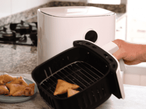 Hand holding a black tray with cooked food from a white air fryer.