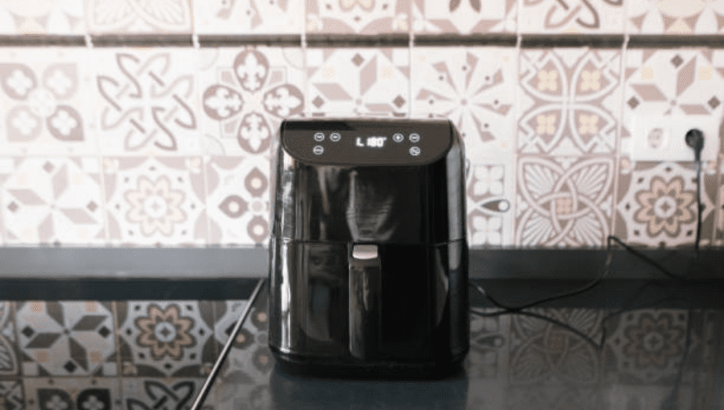 A black air fryer sitting on a kitchen countertop with decorative tile in the background.