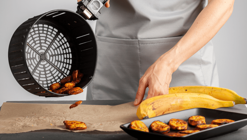 A person serving plantains from an air fryer basket onto a plate.