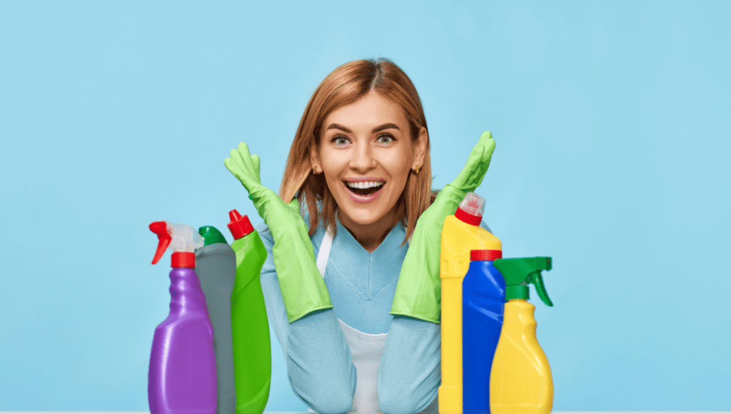 A cheerful woman wearing green gloves, surrounded by colorful cleaning bottles.