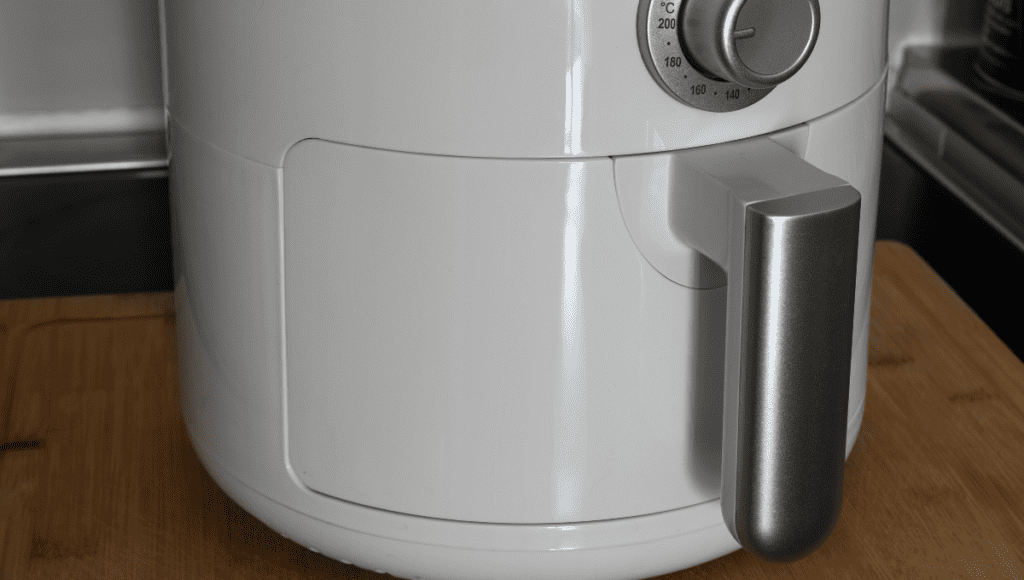 A close-up of a white air fryer set on a kitchen counter, featuring a sleek handle and temperature dial.