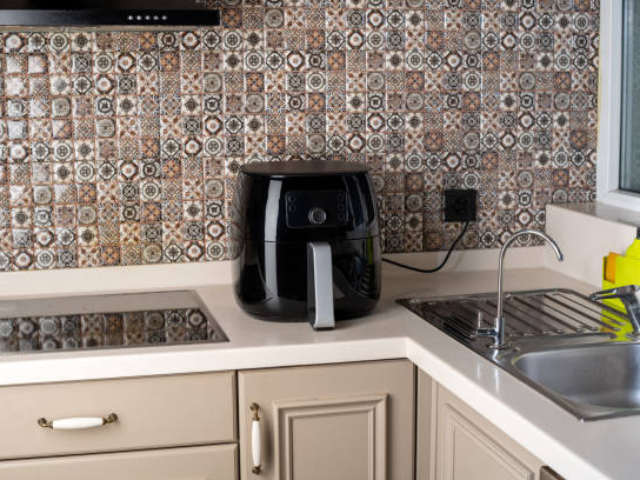 A sleek black air fryer sits on a kitchen countertop with patterned backsplash tiles.