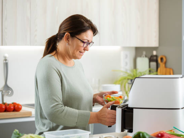 A woman placing vegetables into a white air fryer in her kitchen, ready to prepare a healthy meal.