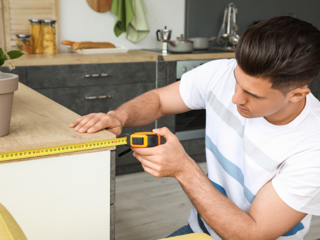 A man using a tape measure to take measurements on a kitchen counter.