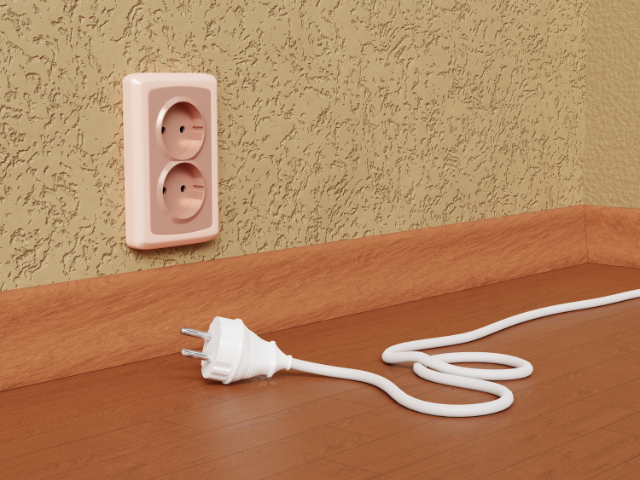 A power outlet with an unplugged cord laying on the floor.