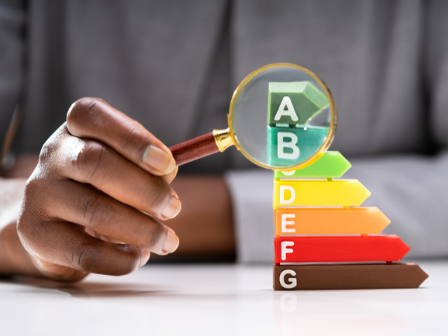 A hand holding a magnifying glass over a bar graph with energy efficiency ratings from A to G, with A being the most efficient.