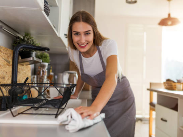 A woman smiling while cleaning the kitchen counter.