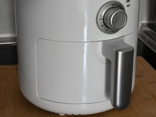 Close-up of a white air fryer on a wooden countertop in a kitchen. The air fryer is set to 180°C on the dial.