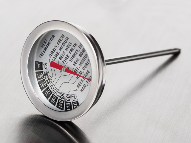 A close-up of a meat thermometer with specific temperature zones for various types of meat like beef, pork, lamb, and turkey.