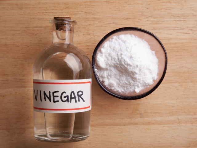 A bottle of vinegar and a bowl of baking soda on a wooden surface.