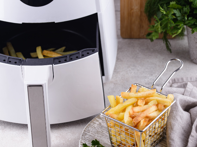  A white air fryer next to a small basket of freshly cooked golden French fries.