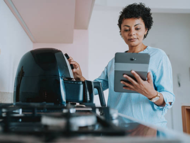 A woman checking a recipe on her tablet while cooking with an air fryer in a modern kitchen.