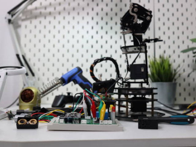 Various electronic components, wires, and a robotic arm on a workbench, showcasing a DIY or tech project setup.