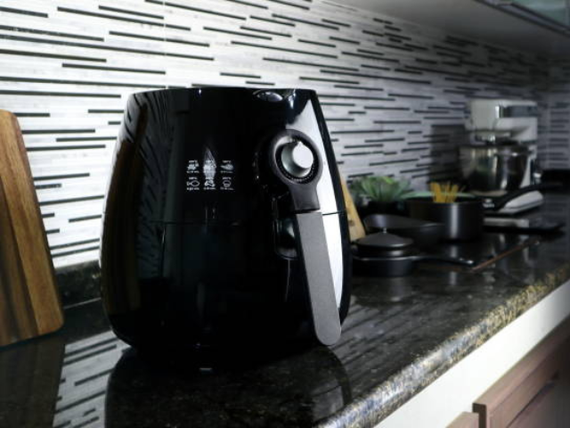 Black air fryer on a granite countertop in a modern kitchen with a striped tile backsplash.