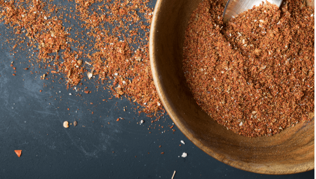 A bowl of spice blend scattered on a dark background.