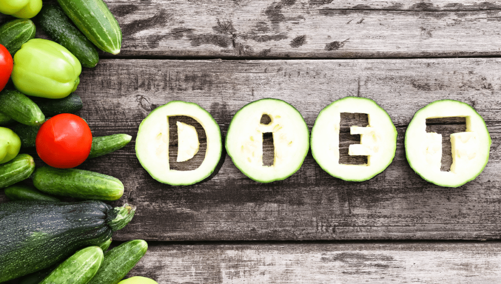 The word 'DIET' spelled out with cucumber slices, surrounded by fresh vegetables.