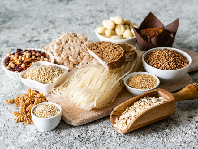 A selection of grains, pasta, bread, and rice cakes arranged on a rustic surface.