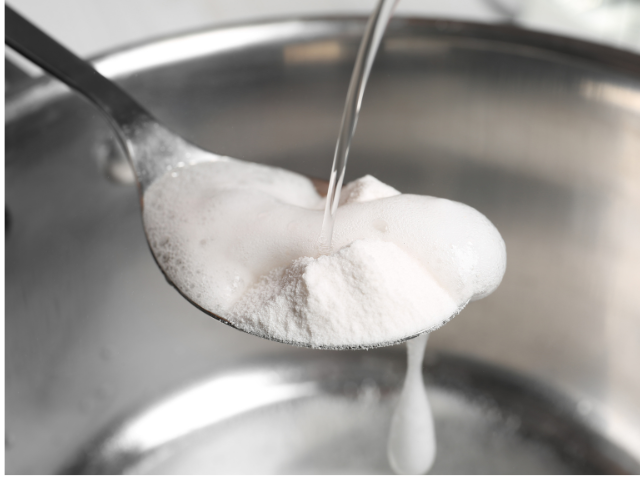 A spoon of baking soda being mixed with water in a metal bowl.