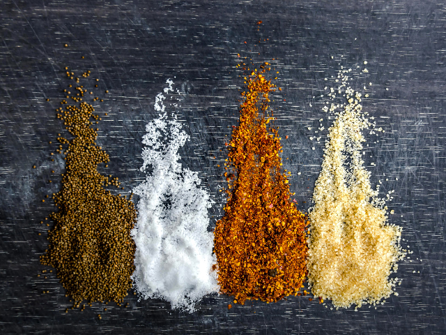 Various spices including mustard seeds, salt, and pepper flakes in a creative display.